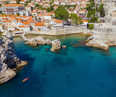 Kayaks glide across blue water, moving away from historic city walls and orange-roofed buildings
