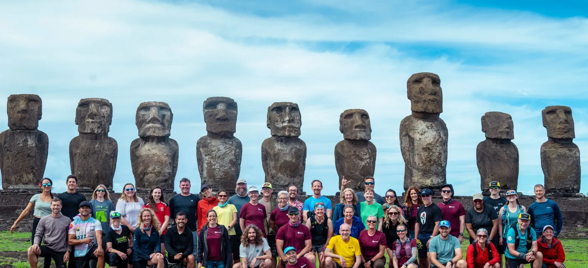 Group of smiling participants in colourful clothes with statues behind them and a blue sky above