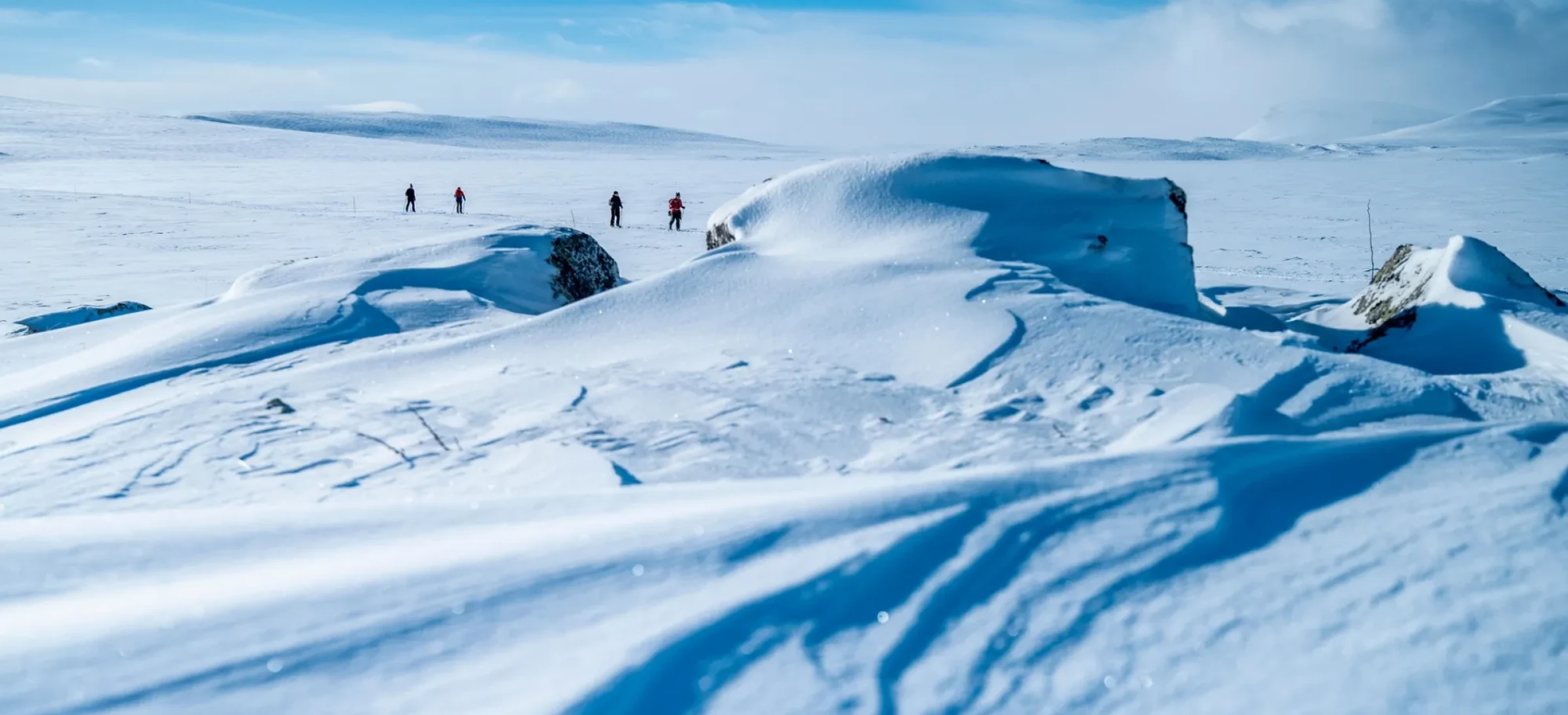 Participants crossing vast, snowy terrain under a bright blue sky