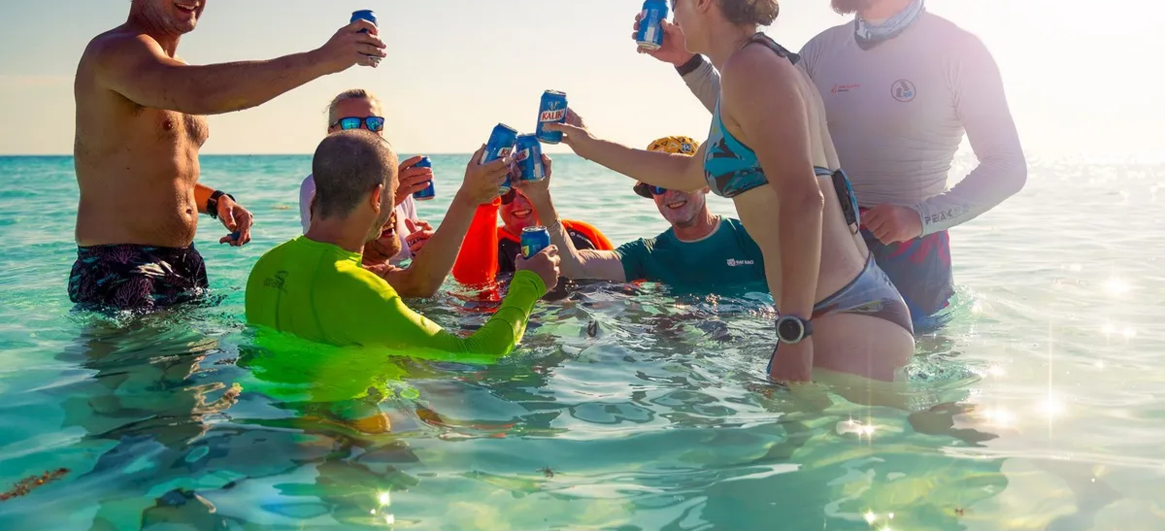 Group of people stood in clear water and celebrating with a canned drink