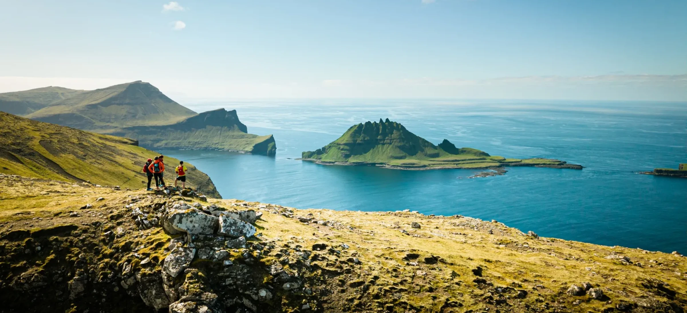 Participants stand on rocky ledge, looking out to cliffs and clear, blue waters