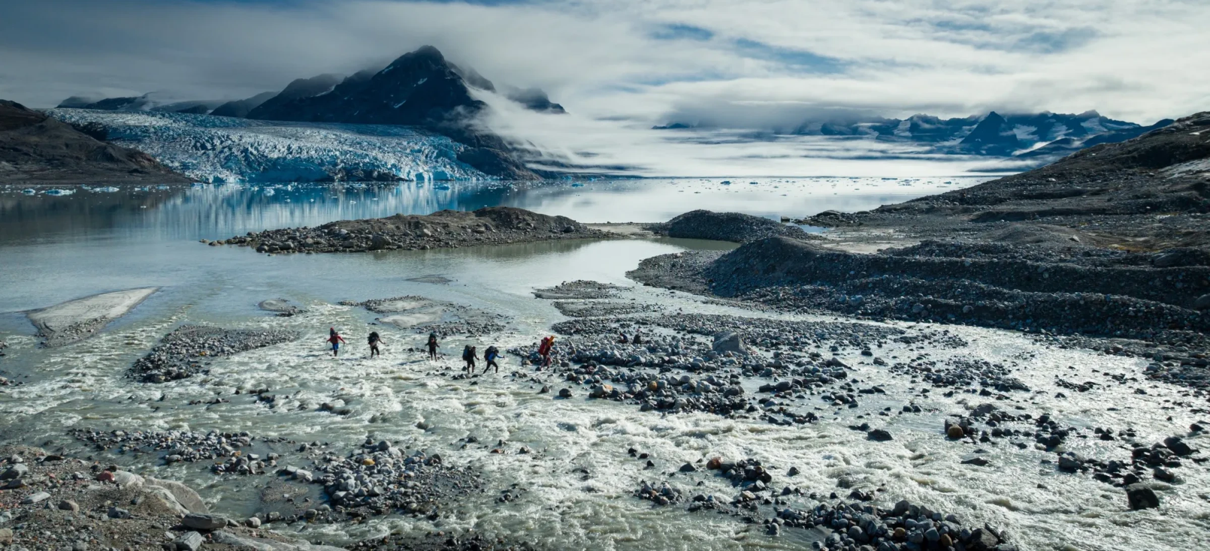 Participants walking across frozen water and rocky terrain with blue and cloudy sky above
