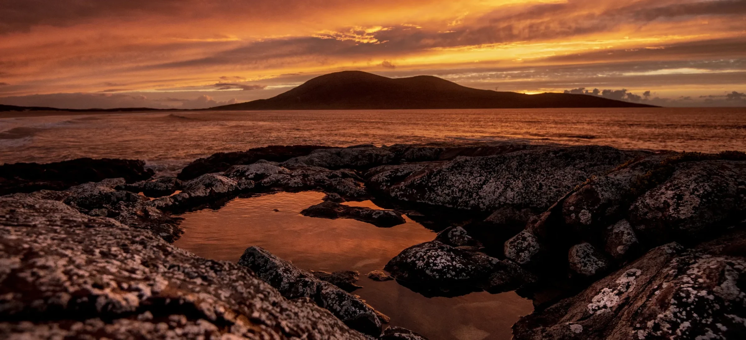 Rocky shoreline and colourful sky with hills in the background