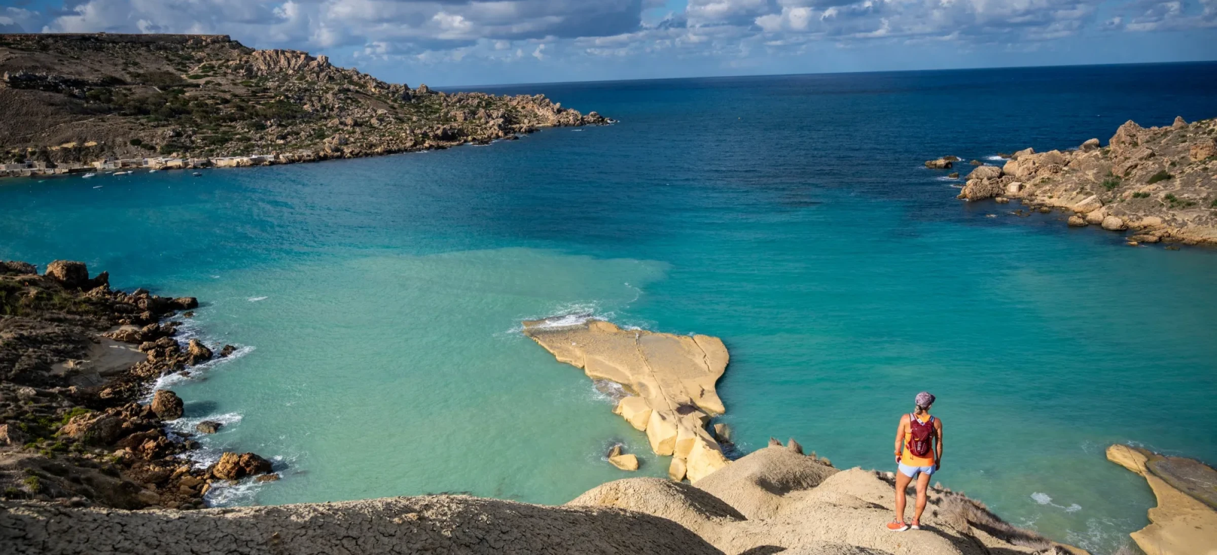 Woman stood on rocks, looking out to clear, still sea