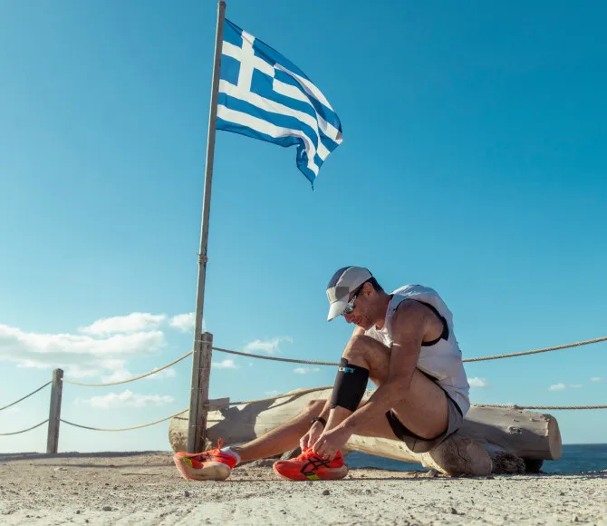 Man sat, tying shoe laces with Greek flag next to him