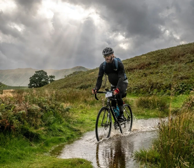 Man cycling through water with greenery either side of him