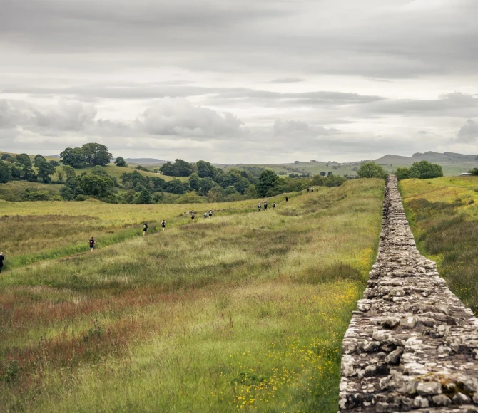 People running through fields, past Hadrain's Wall
