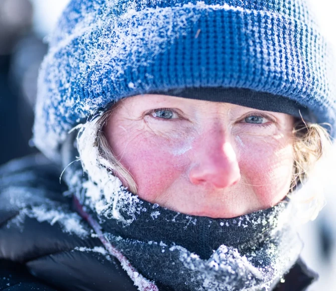 Woman wearing beanie hat and warm clothes covered in snow and ice