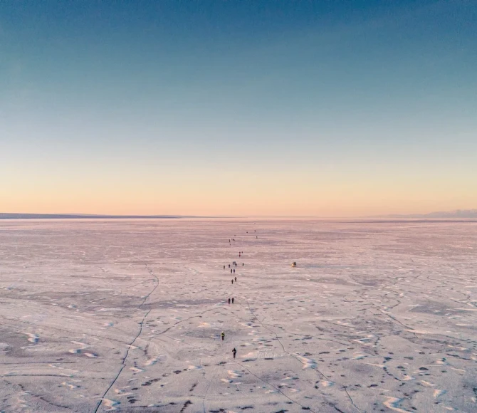 Participants walking on frozen ground with colourful sky above