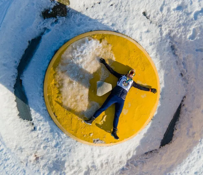 Rat Race Participant lying with their arms out and face up on a bright yellow circle, surrounded by snow