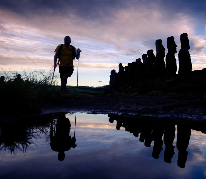 Silhouette of a man running through water, with statues to his left and a colourful sky behind