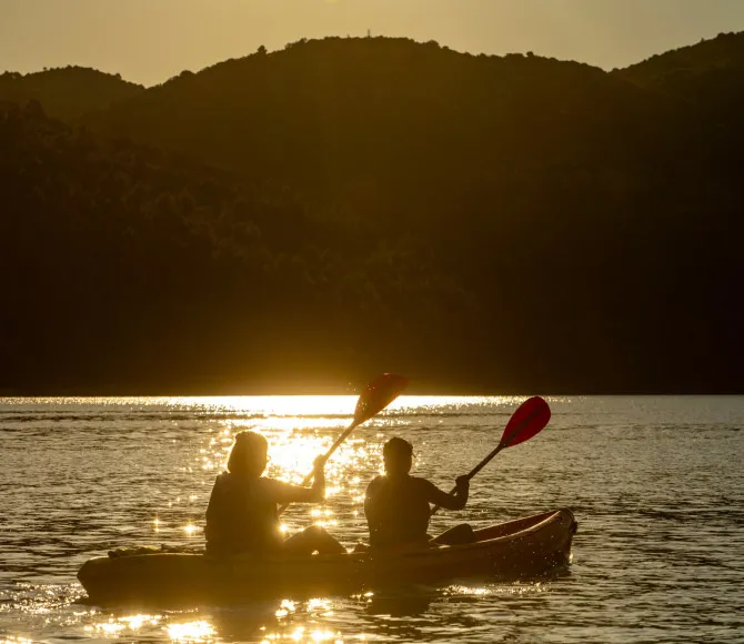 Two participants kayak towards the sunlit horizon, with rolling hills lining the water in the distance