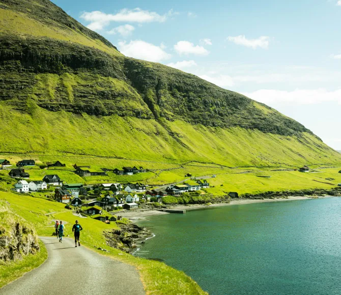 Participants running along sunlit coastal path with houses in the distance