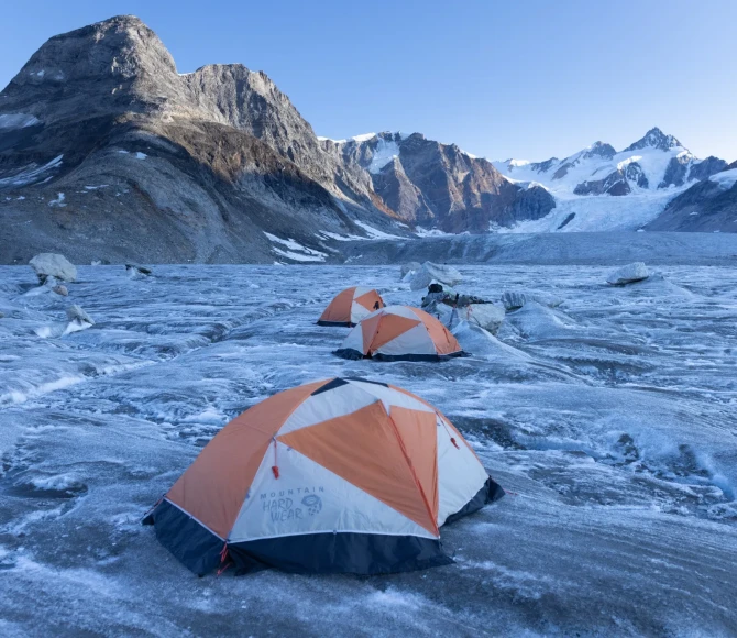 Three tents pitched on snowy and icy terrain with mountains in the background