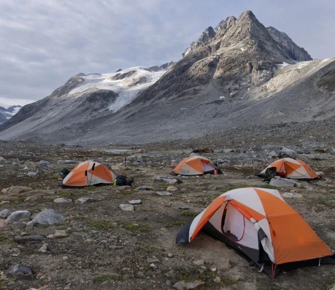 Four colourful tents pitched on rocky terrain with mountains in the background