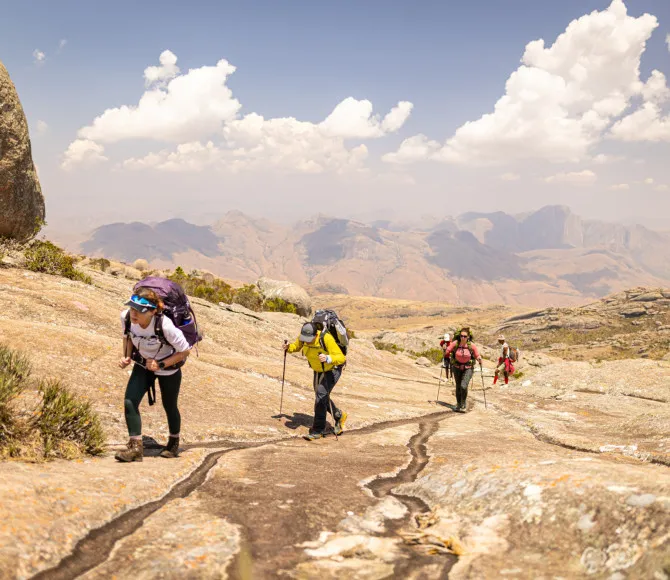 Participants walking with trekking poles over sand-coloured ground with the bright sky above them