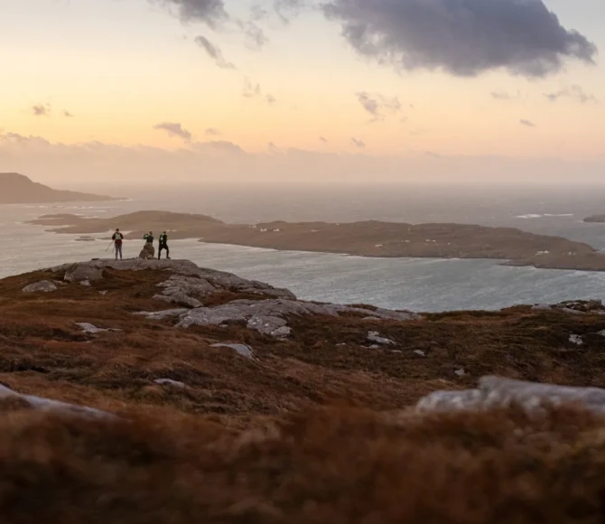 People stood on rocky coast with colourful sky above