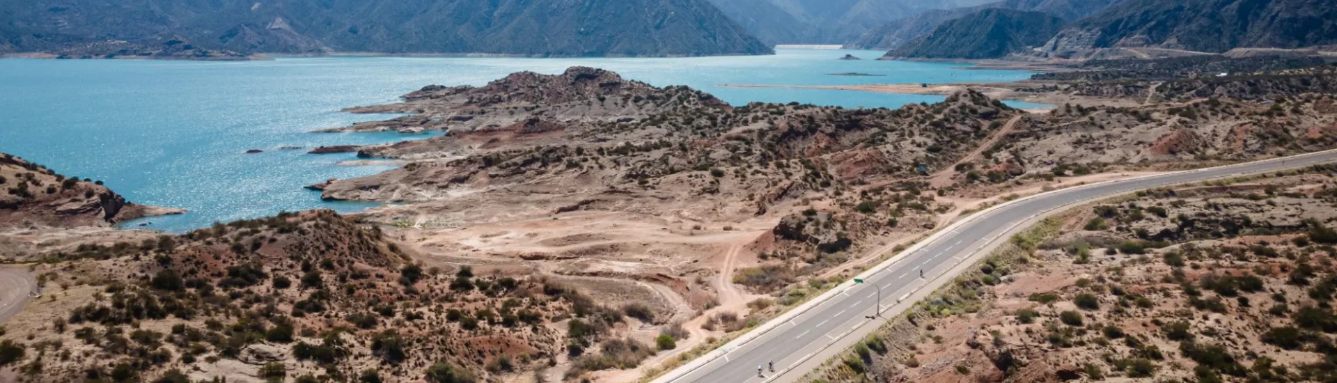 Cyclists riding along road with water and mountains behind