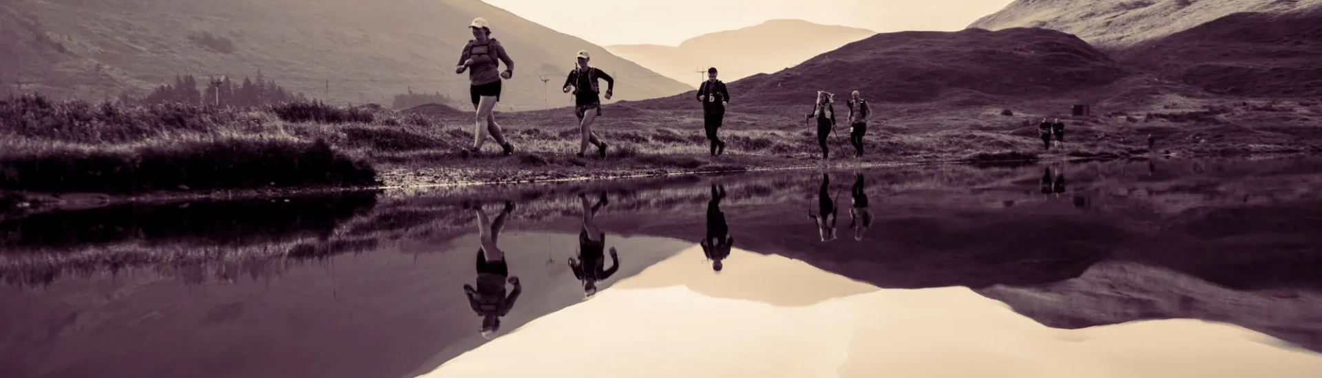 People running past still water with mountains in background