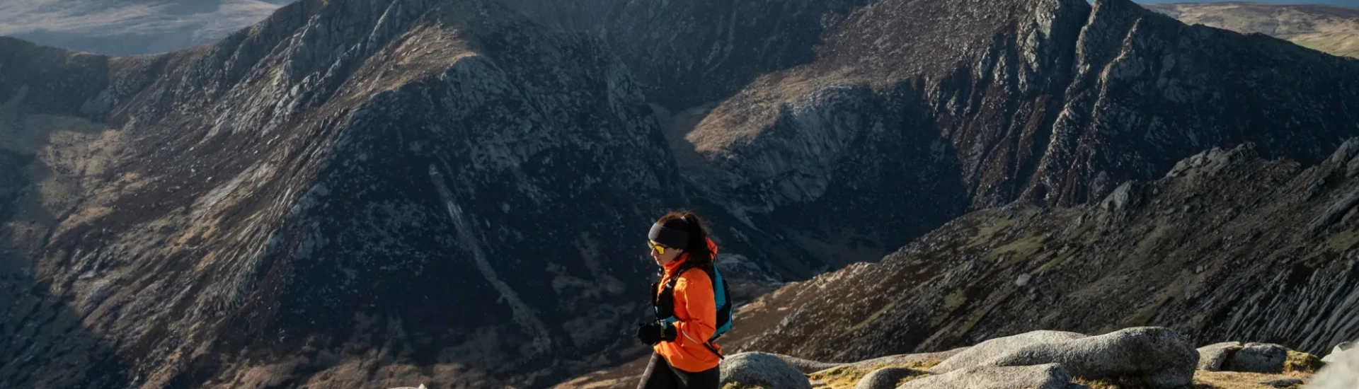 Woman running over grassy terrain with mountains in the background