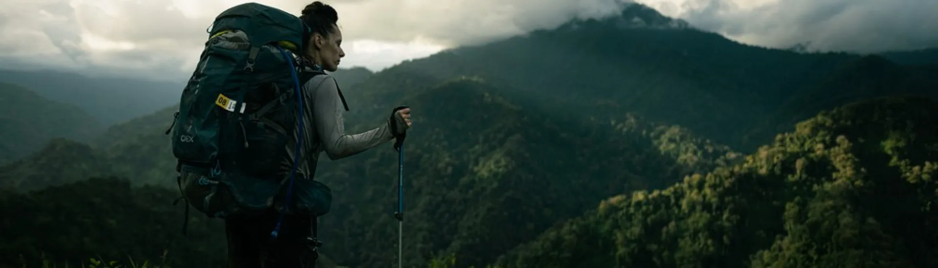 Woman wearing a large rucksack and carrying trekking poles stood looking out to dense jungle