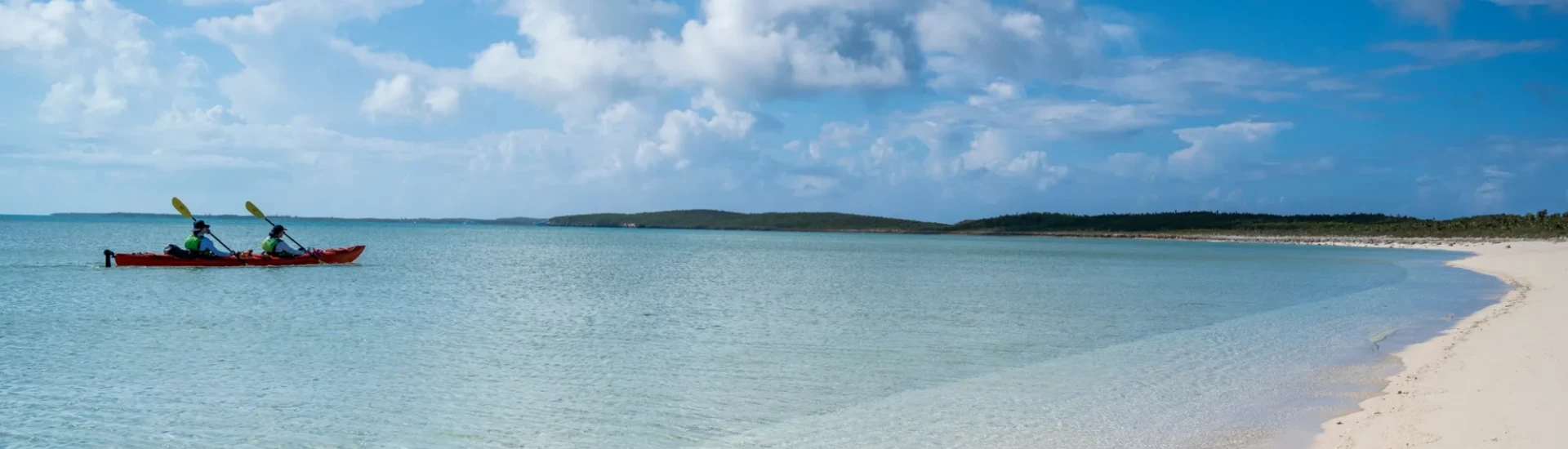 Two participants kayaking through shallow water near a sandy beach