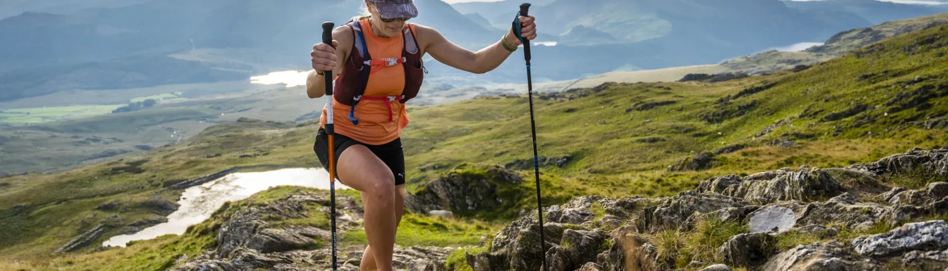 Woman using trekking poles and climbing over rocks and grass