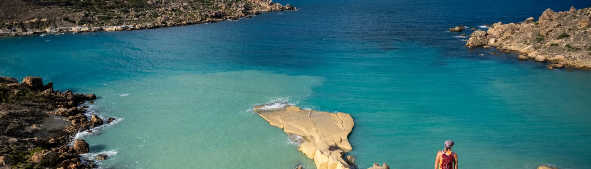 Woman stood on rocks, looking out to clear, still sea