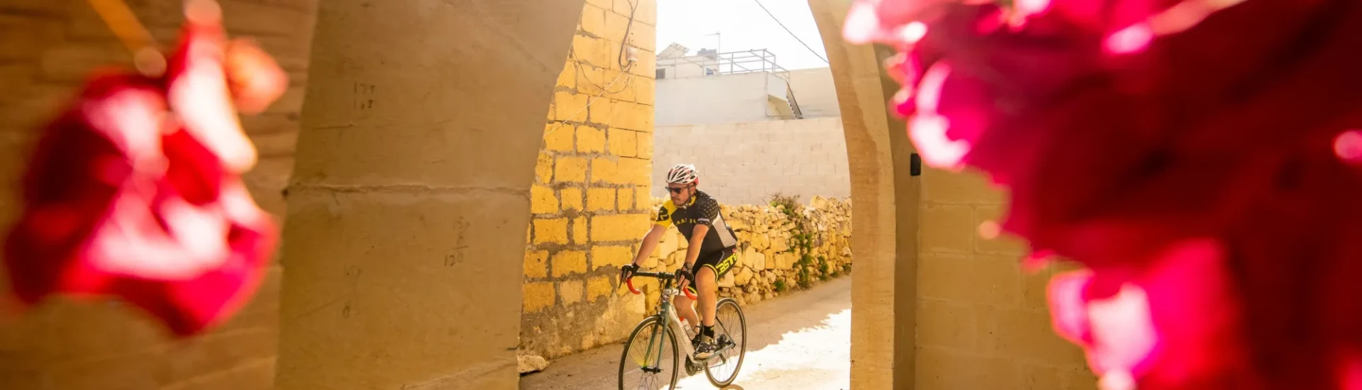 Cyclist rides past archway, leading to colourful flowers