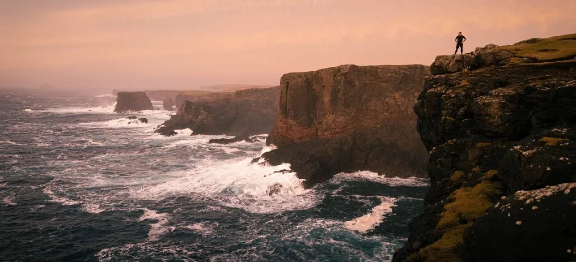 Person stood on cliff with colourful sky above them