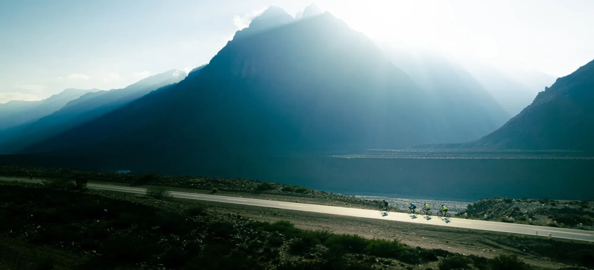 Cyclists riding along road past mountains