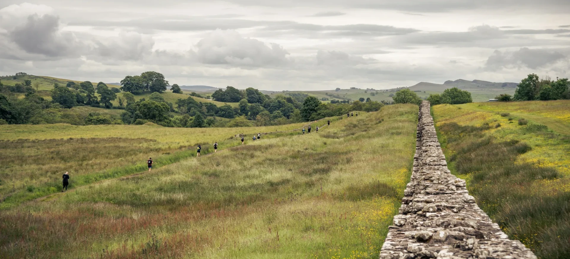 People running through fields, past Hadrain's Wall