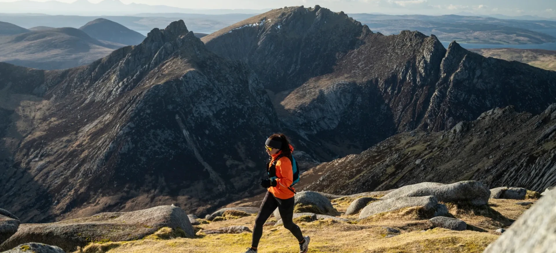 Woman running over grassy terrain with mountains in the background
