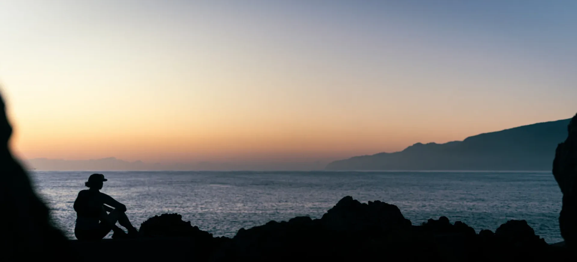 Participant sat on rocks, looking out to sunset over sea