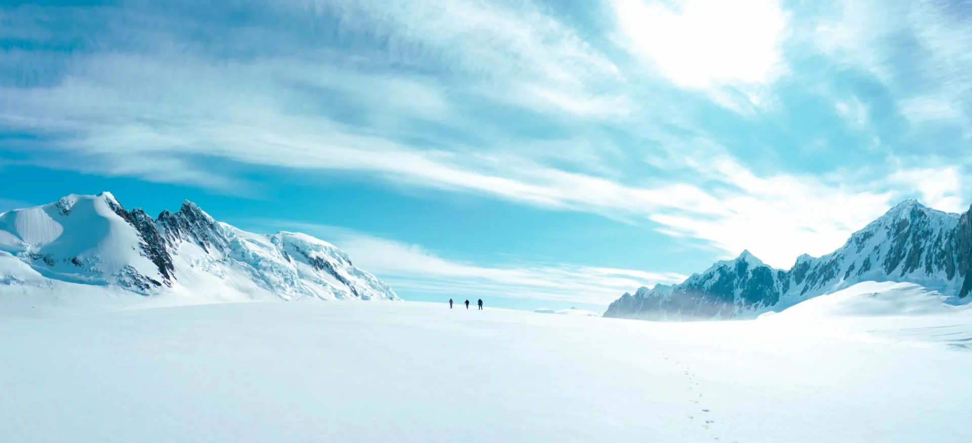 A snowy Antarctic setting with snow-covered mountains either side and participants far in the distance