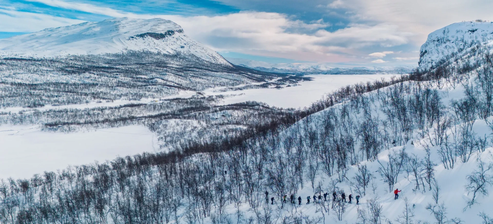 Group of participants making their way through a snowy forest with mountains in the background
