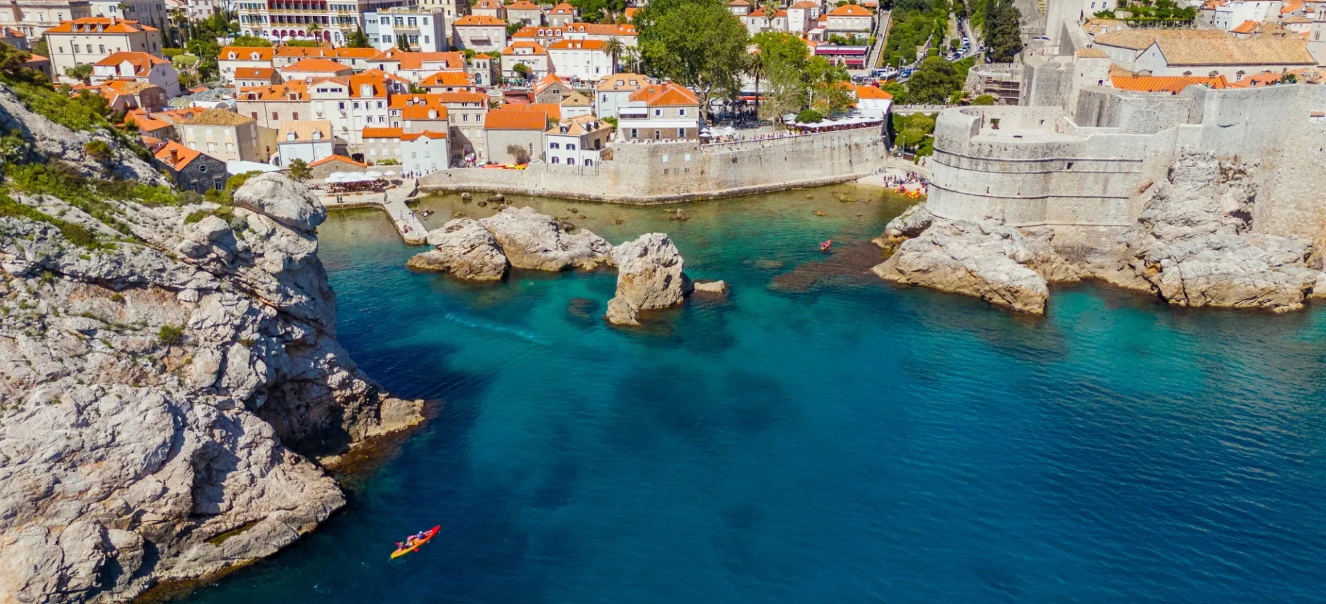 Kayaks glide across blue water, moving away from historic city walls and orange-roofed buildings