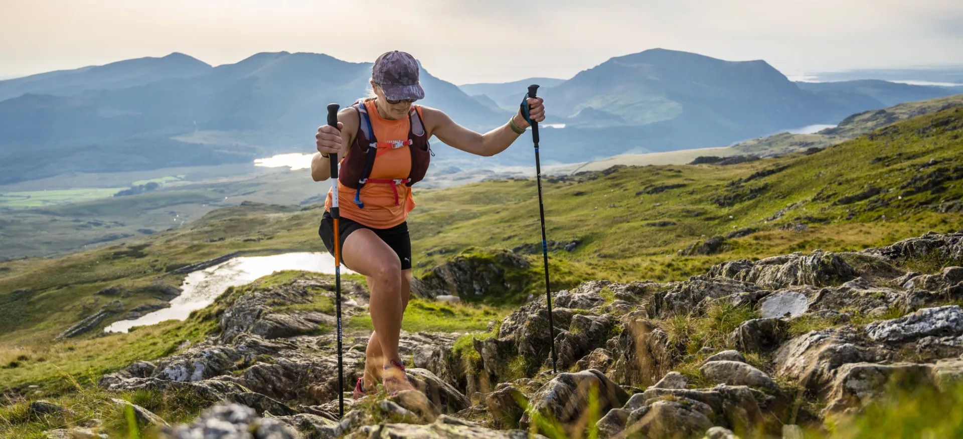 Woman using trekking poles and climbing over rocks and grass