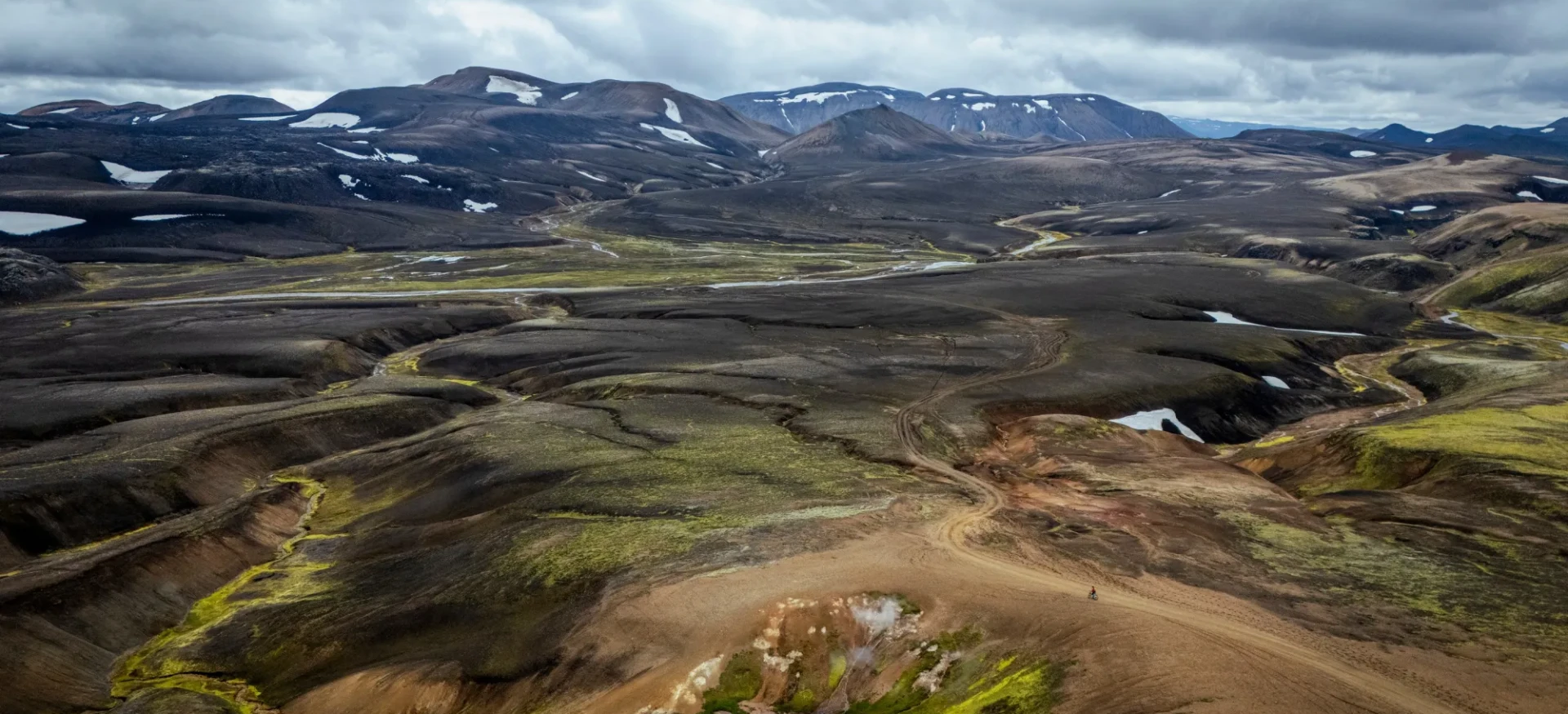 Cyclist riding over dark, rocky terrain with sparse patches of greenery
