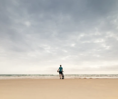 Woman standing on sandy beach with bike