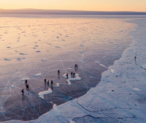Participants walking along frozen lake with colourful sky above