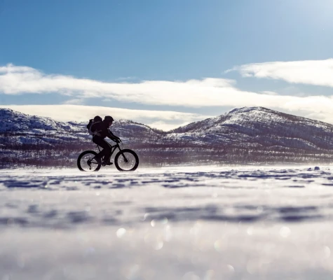 Single cyclist riding across a snowy landscape on a fat bike