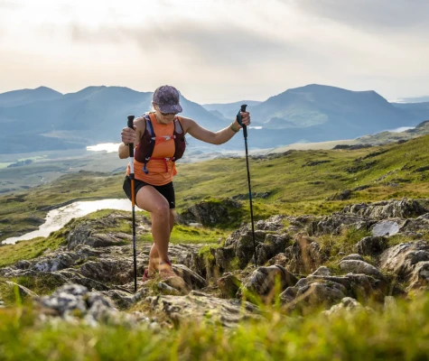 Woman using trekking poles and climbing over rocks and grass