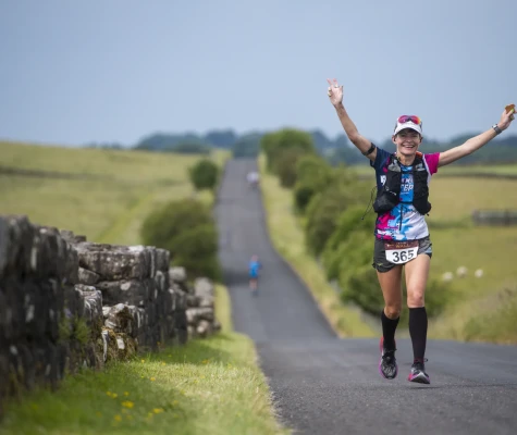 Woman running along wall, smiling with her hands in the air