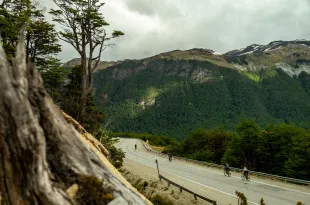 Cyclists travelling along road surrounded by mountains and greenery