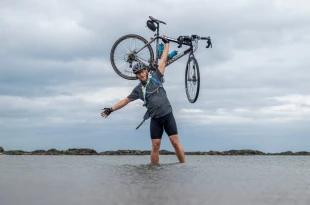 Man stood in water and holding his bike above his head