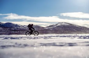 Single cyclist riding across a snowy landscape on a fat bike