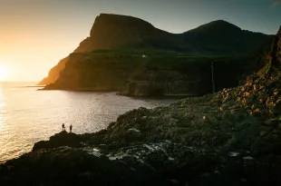 Participants stood on rocky terrain, looking out to sea at sunset
