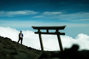Woman stood on rocky terrain, looking out to bright sky and clouds