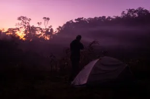 Participant stood by tent, looking out to purple, colourful sky